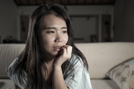 年轻伤心沮丧的亚裔韩国妇女绝望地哭着坐在家里沙发沙发上饱受抑郁