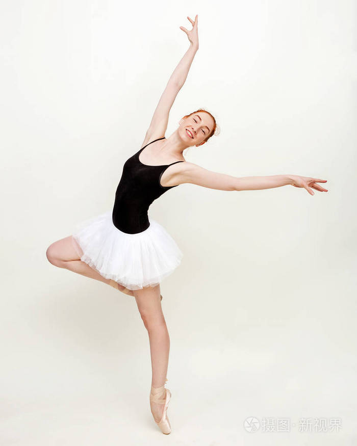 这位年轻美丽的芭蕾舞演员在一间光线充足的浅灰色工作室里摆姿势跳舞