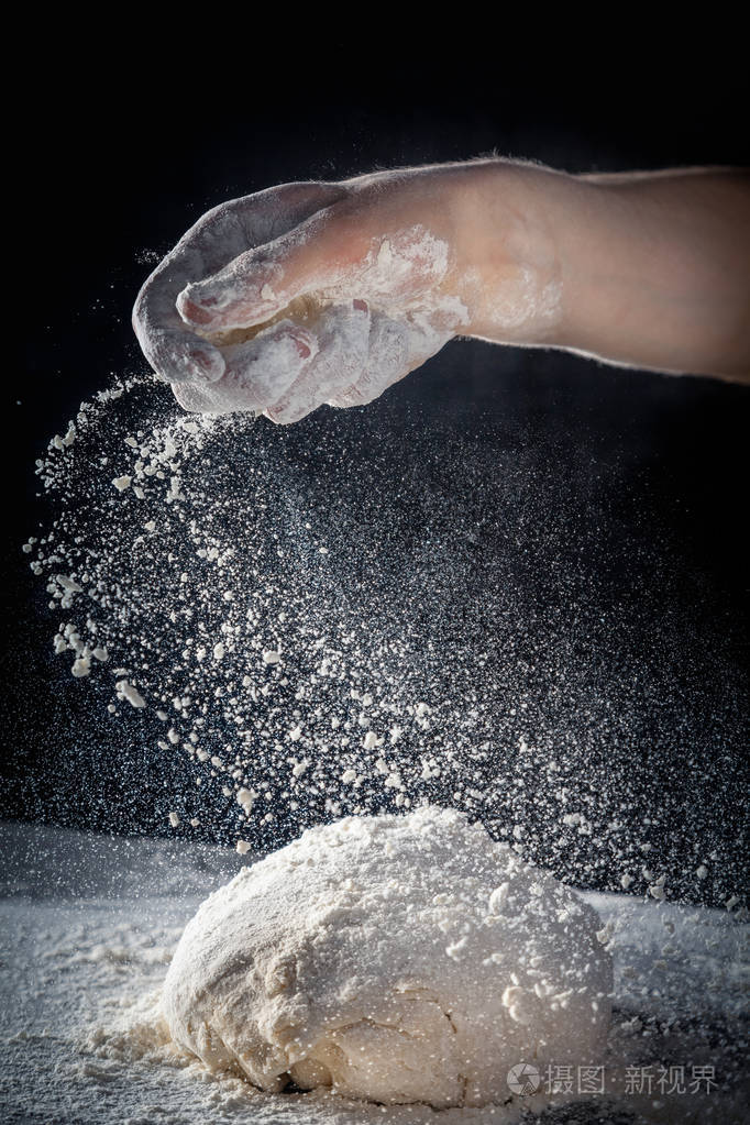厨师用面粉做面团把面粉撒在桌子上深色背景上的面团上垂直的复制空间