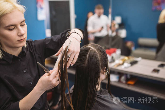 年轻的美女在美容院理发.用剪刀剪头发的过程.理发师修剪棕色.