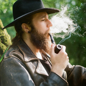 戴帽子的大胡子男人抽烟斗的肖像.照片