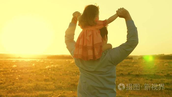 爸爸在阳光下和女儿在肩上跳舞在夕阳的余晖中父亲扛着孩子旅行孩子和