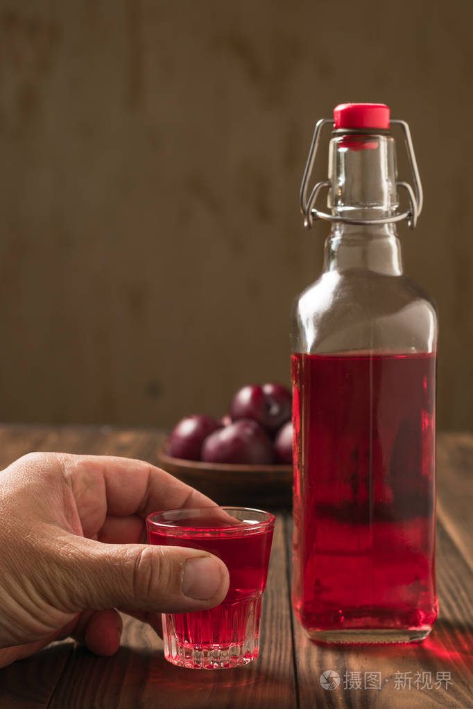 一个男人拿着一杯李子利口酒靠近瓶子