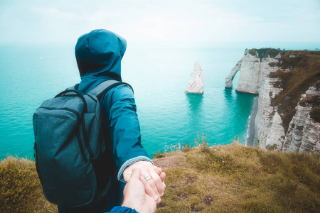 身穿雨蓝雨衣的年轻女子牵着男朋友的手,领着他到悬崖边看海景.