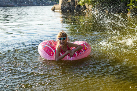 穿着粉红色泳衣，戴着充气环的孩子在河里游泳。照片