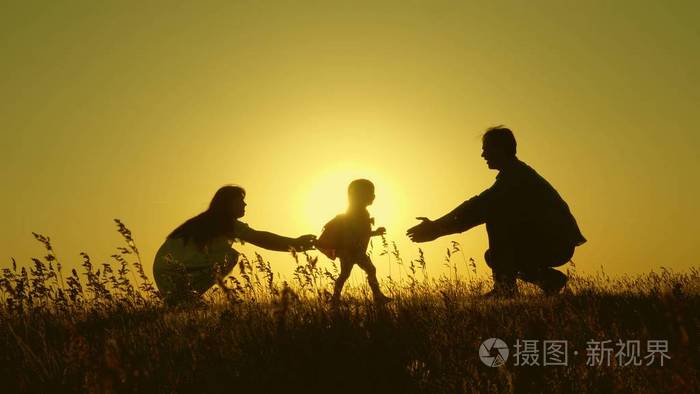 小女儿和父母在夕阳下跳跃.晨曦中爸爸妈妈和宝宝的剪影.家庭观念.