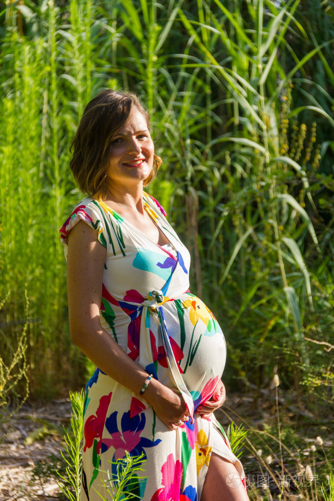 一个穿着五颜六色衣服的年轻孕妇在公园里摆姿势