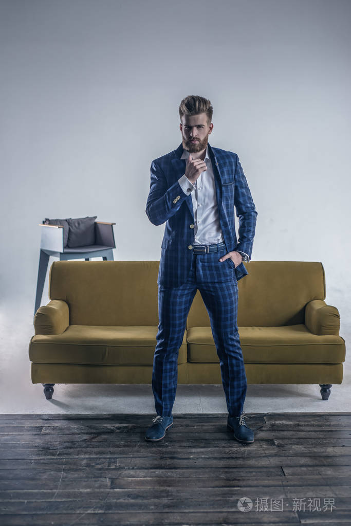 一个穿着全套西装和吊带的帅哥站在房间里看着镜头双手托着下巴