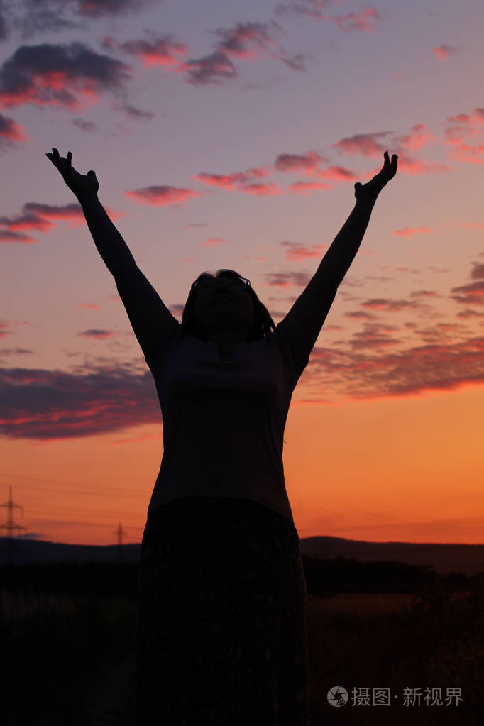 一个女人的黑影,她举起双手向天空举起,美丽的粉红色夕阳和紫色的云朵