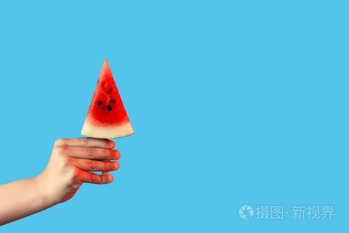 手拿着一块西瓜放在蓝色背景的冰激凌上