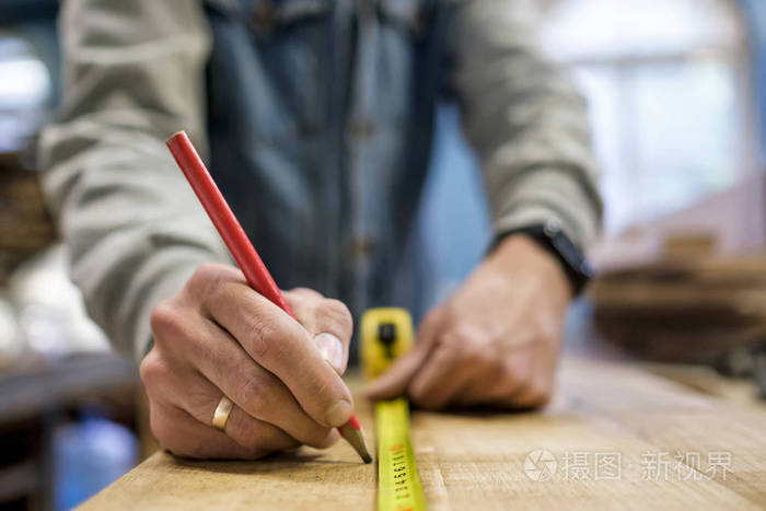 木匠用尺子和铅笔在木头上测量和画线。