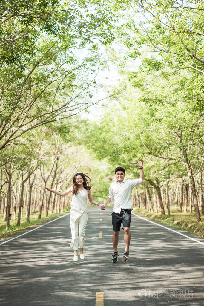 幸福的亚洲情侣在树拱门的路上相爱