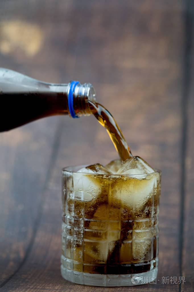 用手将软饮料倒入装有冰块的玻璃杯中