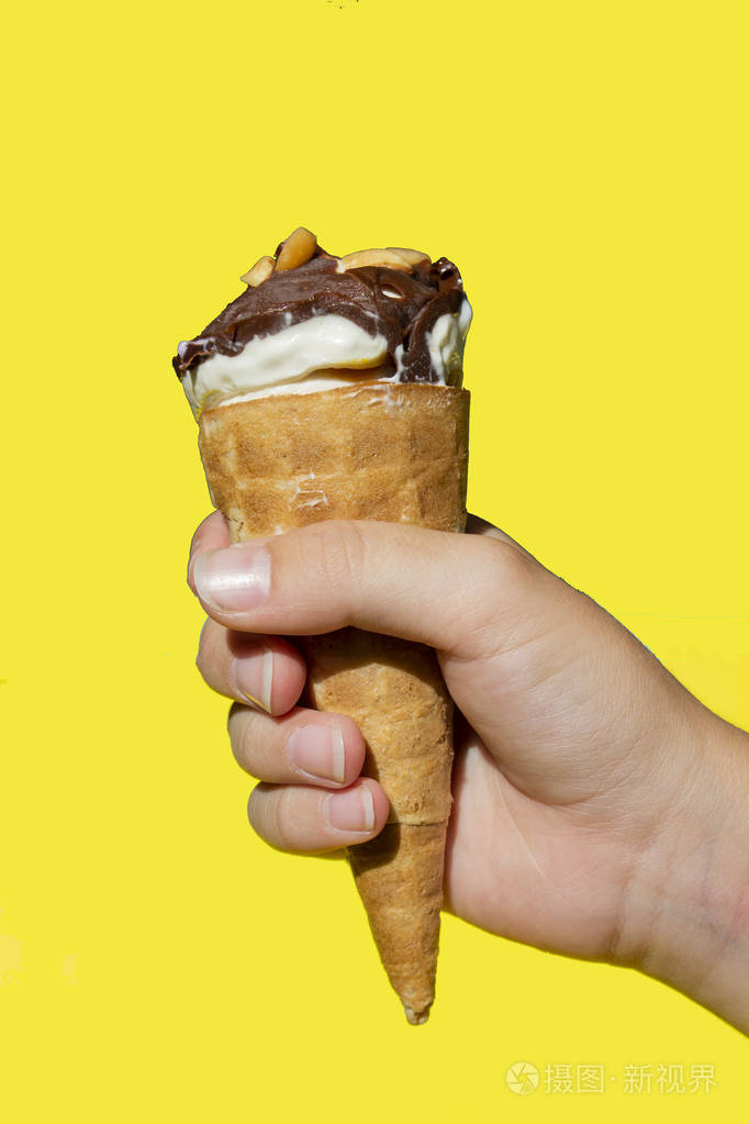 孩子的手拿着一个黄色背景的冰淇淋汉