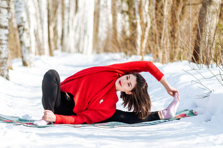 在公园里练习瑜伽的女孩.每年的冬天.白雪覆盖的树木.照片