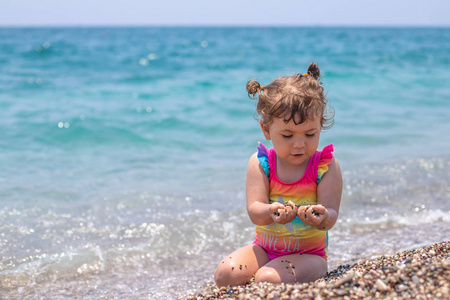 一个穿着彩色泳衣的小女孩坐在海边.女孩在海滩上玩.