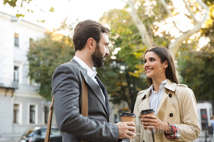 照片中微笑的上班族男女在城市街道开会时喝着外卖咖啡