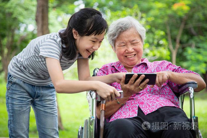 快乐的亚洲老奶奶和小女孩一起用手机在智能手机上玩电子游戏轮椅上