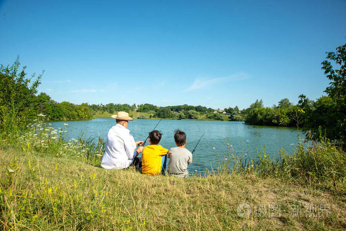 两个拿着钓竿的男孩和爷爷在池塘里钓鱼