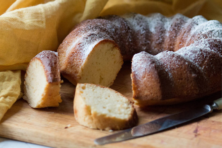 the round sweet cake strewed with icing sugar on a wooden board