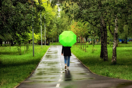 夏天,在城市公园里,一个年轻漂亮的女孩在绿伞下独自行走照片