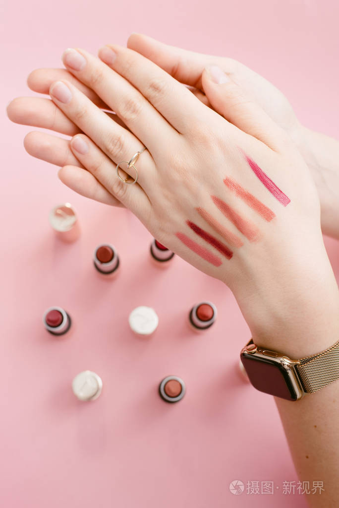 斯沃琪唇膏在一个女孩的纤细的手上不同的口红样本在粉笔粉红色背景上