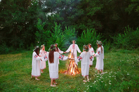 穿着斯拉夫服装的年轻人围着森林里的篝火跳舞.照片