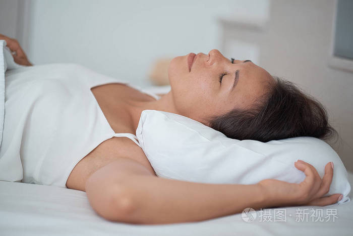 迷人的年轻女子睡在床上抱着柔软的白色枕头少女休息晚安睡眠概念女士