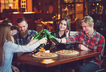 朋友们在酒吧里喝酒,他们坐在一张木桌旁,桌上摆着啤酒和披萨.照片