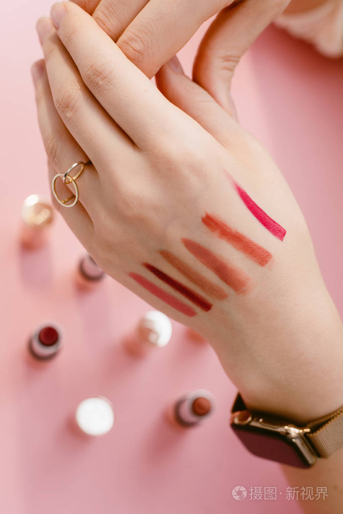 斯沃琪唇膏在一个女孩的纤细的手上不同的口红样本在粉笔粉红色背景上