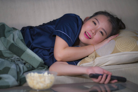看电视剧年轻漂亮,快乐,放松的亚裔中国妇女在家客厅舒适地躺在沙发