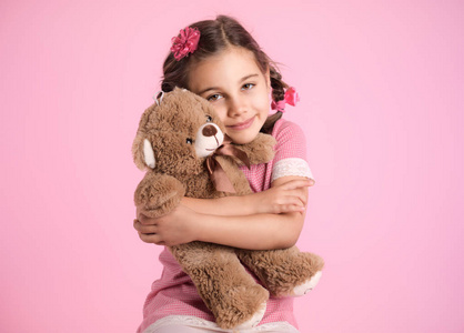 粉红色背景上抱着她柔软的玩具熊的小女孩的肖像照片