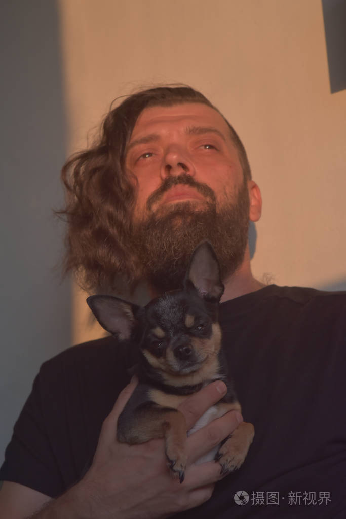 一个留着胡子的男人拥抱着一只小狗品种的吉娃娃