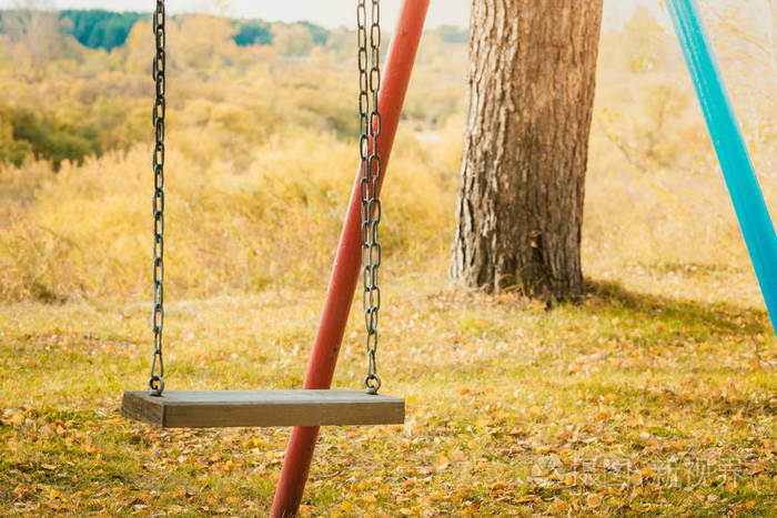 秋天孩子们骑着铁链荡秋千在地上放着黄色的树叶以供骑马和娱乐