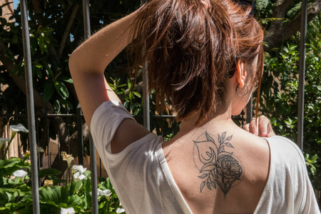 一位年轻的红发游客,背上有一朵海芋百合的纹身,她看着一座花园里开着