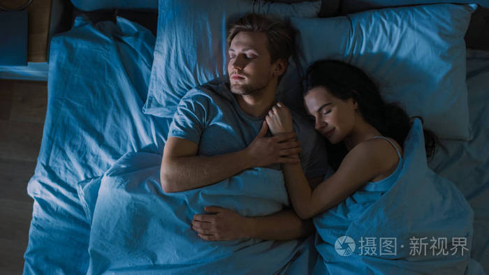 晚上俯视床迷人的年轻夫妇睡在一起抱着对方拥抱第一缕晨光透过窗户
