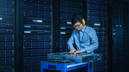 在现代数据中心it技术人员戴着保护性耳机,在安装新硬件的推车上工作.