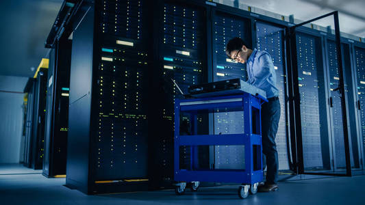 在数据中心:男性it技术员在笔记本电脑上运行维护程序,控制操作服务器