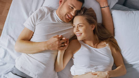 幸福的小夫妻依偎在床上年轻女人怀孕了爱人温柔地抚