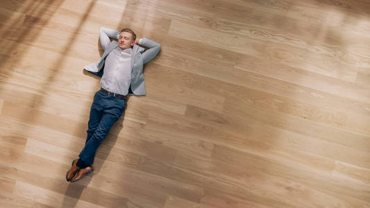 拼花木地板一个年轻人躺在一间公寓的木地板上.他穿着夹克和白衬衫.