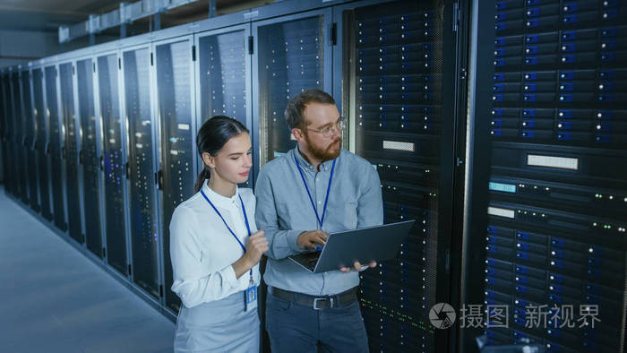 戴着眼镜的留着胡须的it技术人员和一位年轻漂亮的工程师同事正在数据