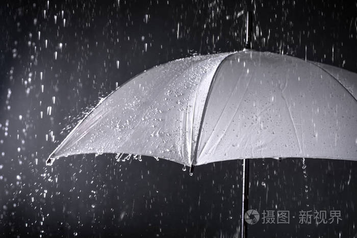 雨中的白色雨伞在黑暗的背景下