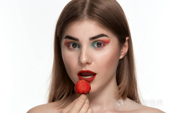 一个美丽的年轻女子的特写肖像色彩鲜艳手持草莓近脸