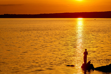 美丽的夕阳在河里,男人拿着鱼竿.照片