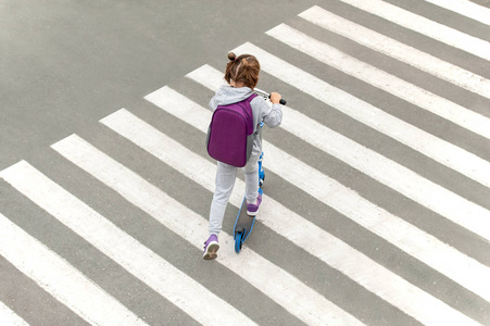 女学生在上学的路上背着滑板车横穿马路.斑马线在城市里步行.