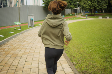 妇女穿连帽衫上衣跑步和慢跑在美丽的城市公园进行健身运动训练照片