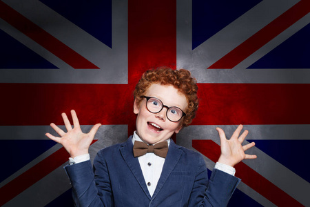 国旗下敬礼英国国旗背景下滑稽调皮的男孩学生照片