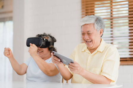 老年时光亚洲老年夫妇在客厅里用平板电脑和虚拟现实模拟器玩游戏