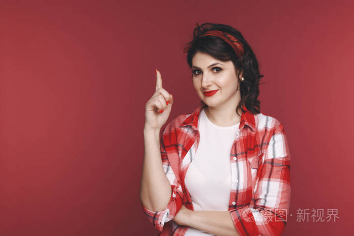 在摄影棚的红色背景上一个迷人的女人用手指指着什么东西