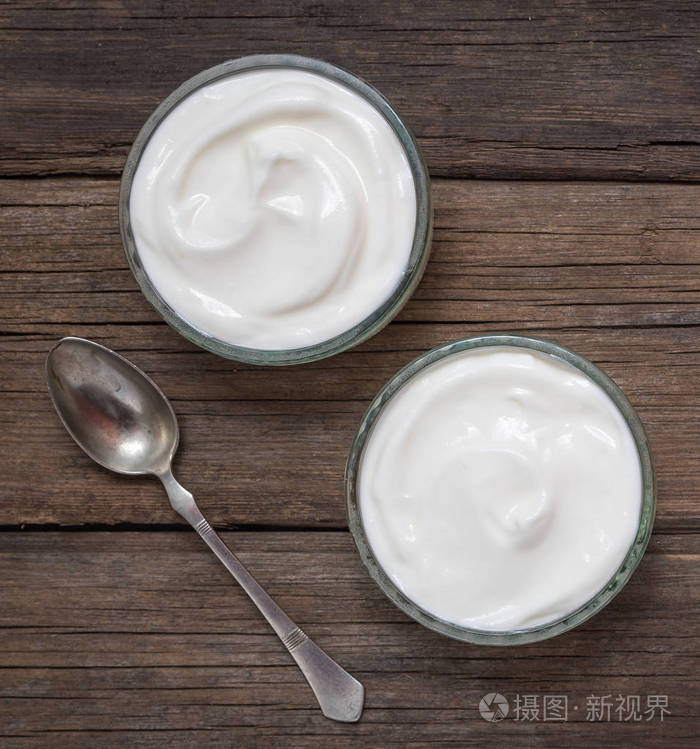 白色酸奶放在旧木桌子上的玻璃碗里配着老式的乡村调羹